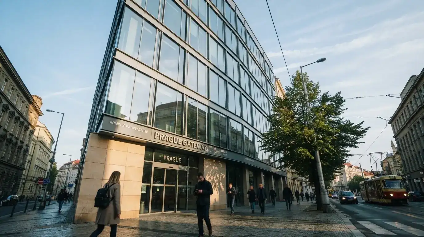 Fasáda moderní administrativní budovy s skleněnými okny odráží ranní oblohu nad rušnou pražskou ulicí.