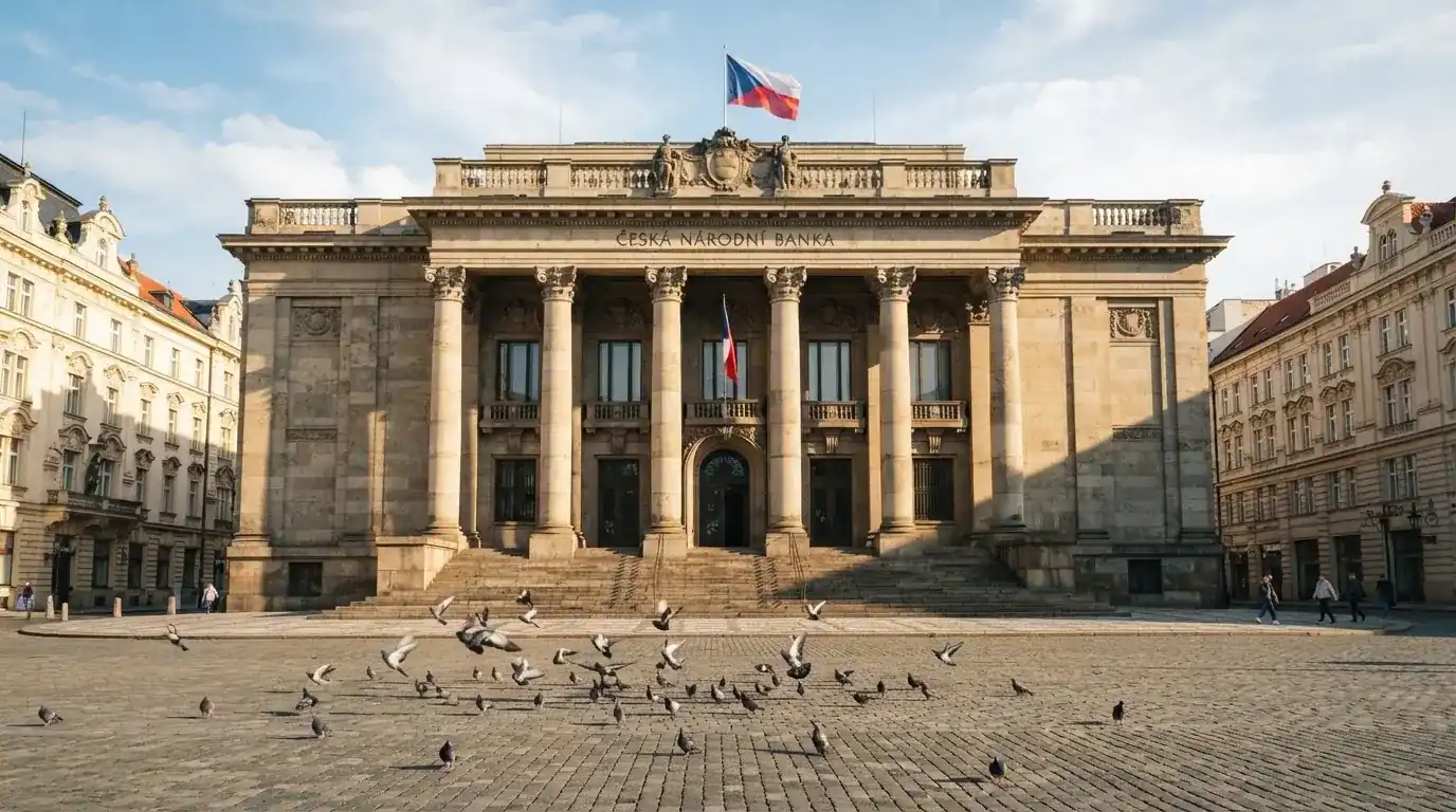 Kamenná budova se sloupy a vlajkou stojí na náměstí za slunečného dne.